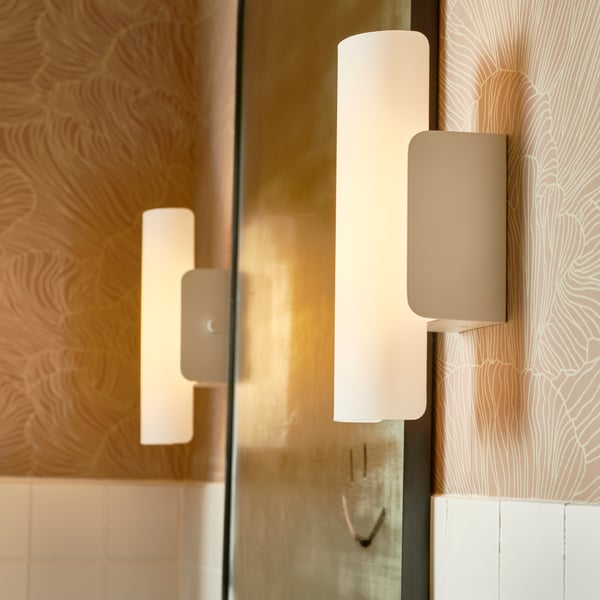 A dimmable matte black KABOMBA LED wall lamp is placed next to a round FAXÄLVEN mirror above a grey washbasin in a bathroom.
