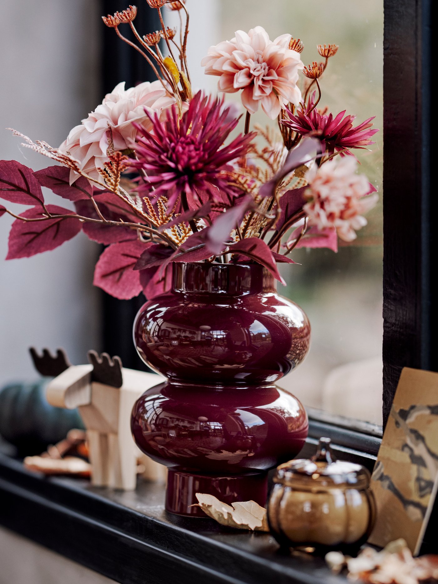A pink SMYCKA artificial bouquet is in a brown-red PÄRLHÄGG vase, along with HÖSTAGILLE decorative items on a windowsill.