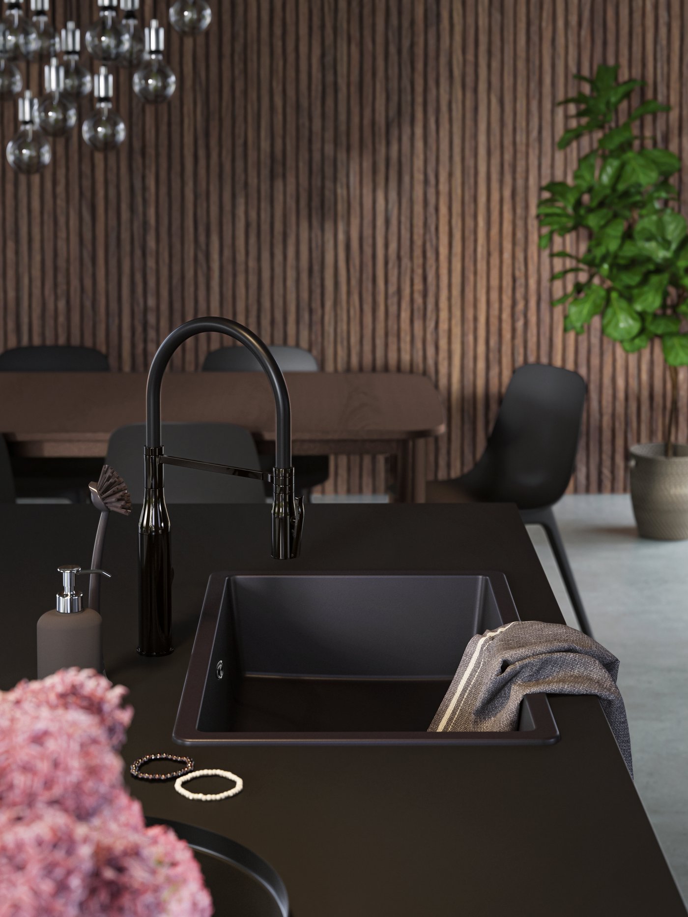 Eine schwarze KILSVIKEN Einsatzspüle auf einer schwarzen EKBACKEN Arbeitsplatte einer Kücheninsel, dazu ein graues Geschirrtuch und ein paar hängende Kräuter.