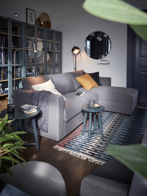 Wohnzimmer mit einem VIMLE 3er-Sofa, hinter dem eine Reihe BILLY Bücherregale mit Glastüren steht. U. a. sind ein LINDBYN Spiegel und ein RESENSTAD Teppich zu sehen.