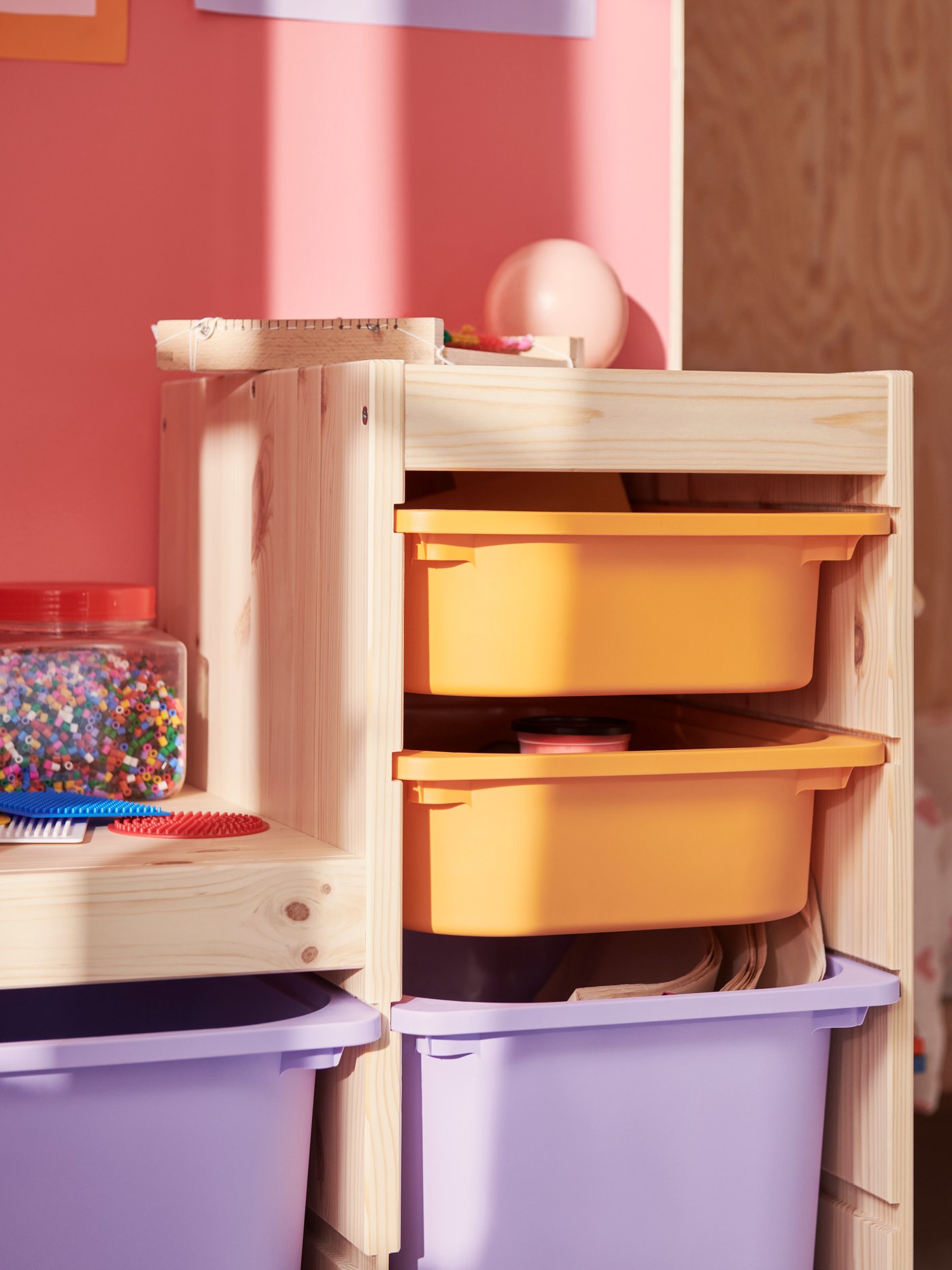 Una struttura TROFAST in pino sbiancato sostiene dei contenitori color arancio chiaro e lilla, pieni di materiale artistico e giocattoli.