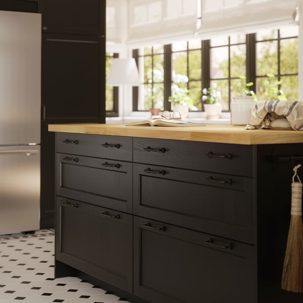 A kitchen with big windows features a large kitchen island with black-stained LERHYTTAN fronts and a bright wooden worktop.