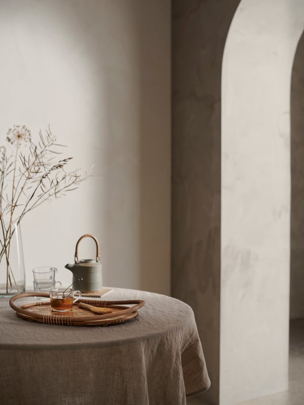 VÅRFINT tray placed on a small round table in a calm dining setting, along with a ceramic teapot and glass mugs.