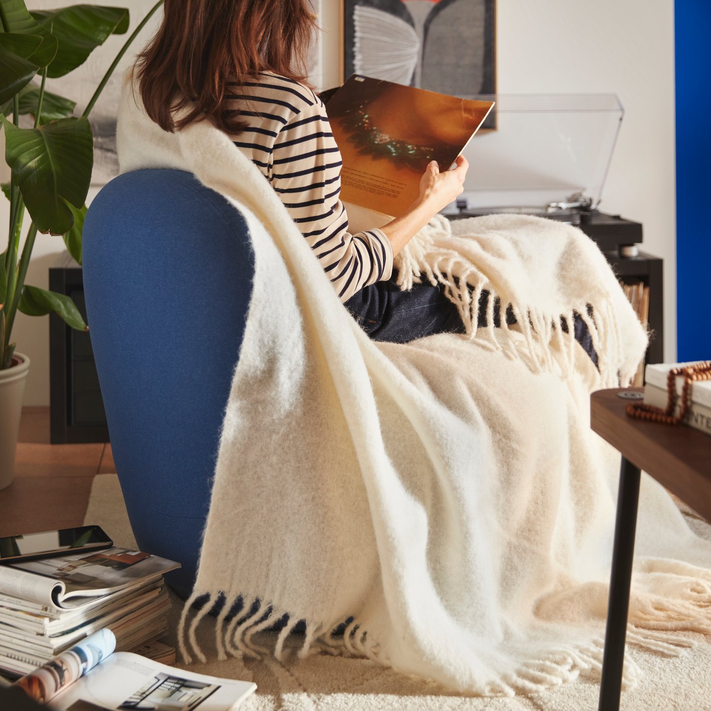 A person sitting on a Gunnared dark blue LILLESÄTER swivel easy chair with a soft KLIPPOXEL throw, next to some magazines.