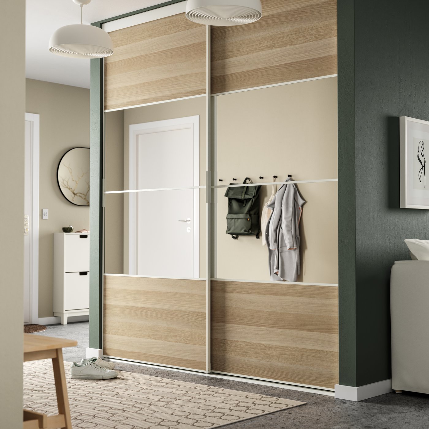 Stilren inredning med SKYTTA garderob i trä och vitt, väggkrokar med kläder, beige väggar, gröna detaljer och abstrakt konst – inspirerande för hall- eller sovrumsdesign.