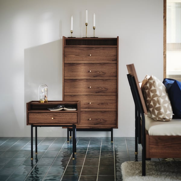 The RÅDMANSÖ series presented with a bedside table and a chest of 5 drawers, standing in a bedroom with blue floor.