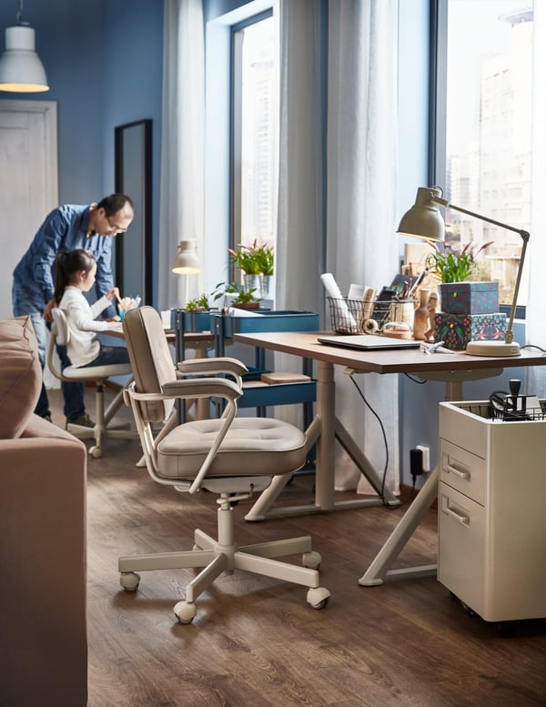 A man and a child in a room with IDÅSEN desks in ash veneer  next to the windows, HEKTAR work lamps and beige office chairs