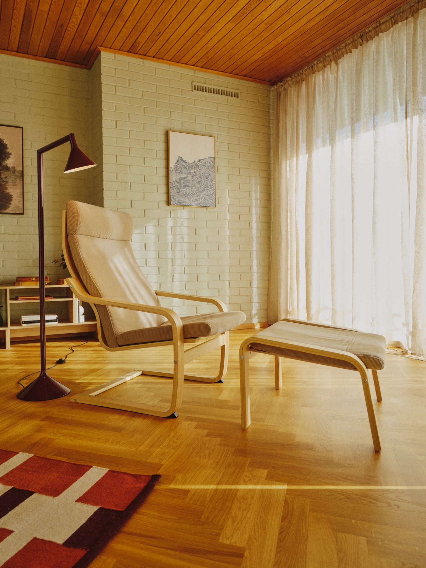 An oak/Kelinge beige POÄNG armchair and matching footstool are in the middle of warm, minimalistic room with wooden floors.