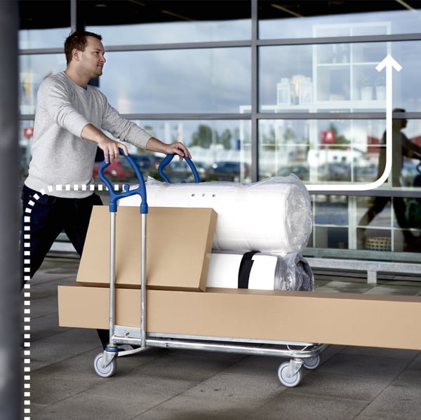 Ein Mann schiebt einen IKEA Lastenwagen voll mit Paketen und Matratzen