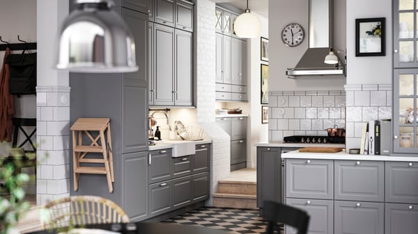 A traditional kitchen with a chequered floor, grey BODBYN kitchen fronts and white/light grey stone effect/laminate worktops.