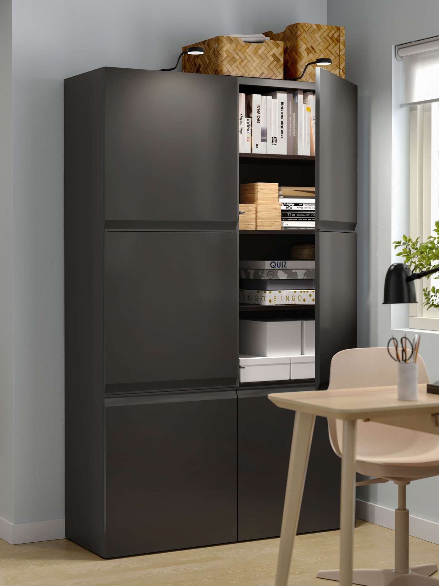 Eine BESTÅ Schrankkombination mit Türen in anthrazit. Davor ein Tisch und ein Stuhl aus hellem Holz.