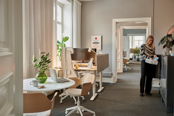 Öppet kontorslandskap med flera skrivbord, stolar och gröna växter, utformat för att ge gott om utrymme och flexibilitet.