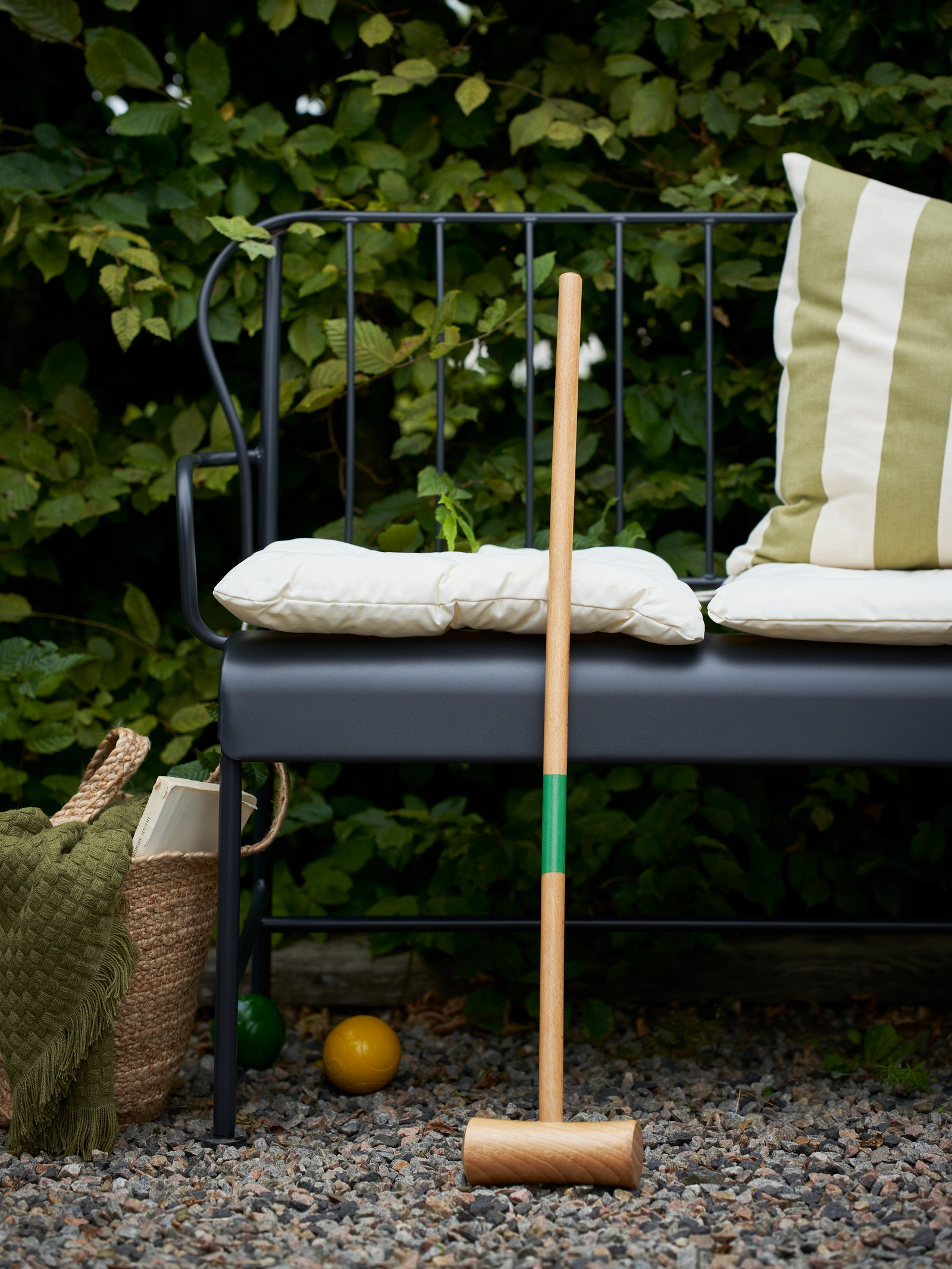 A garden with a cushion in a green natural/striped HILDAMARIA cushion cover on the seat of a grey outdoor LÄCKÖ 2-seat sofa.