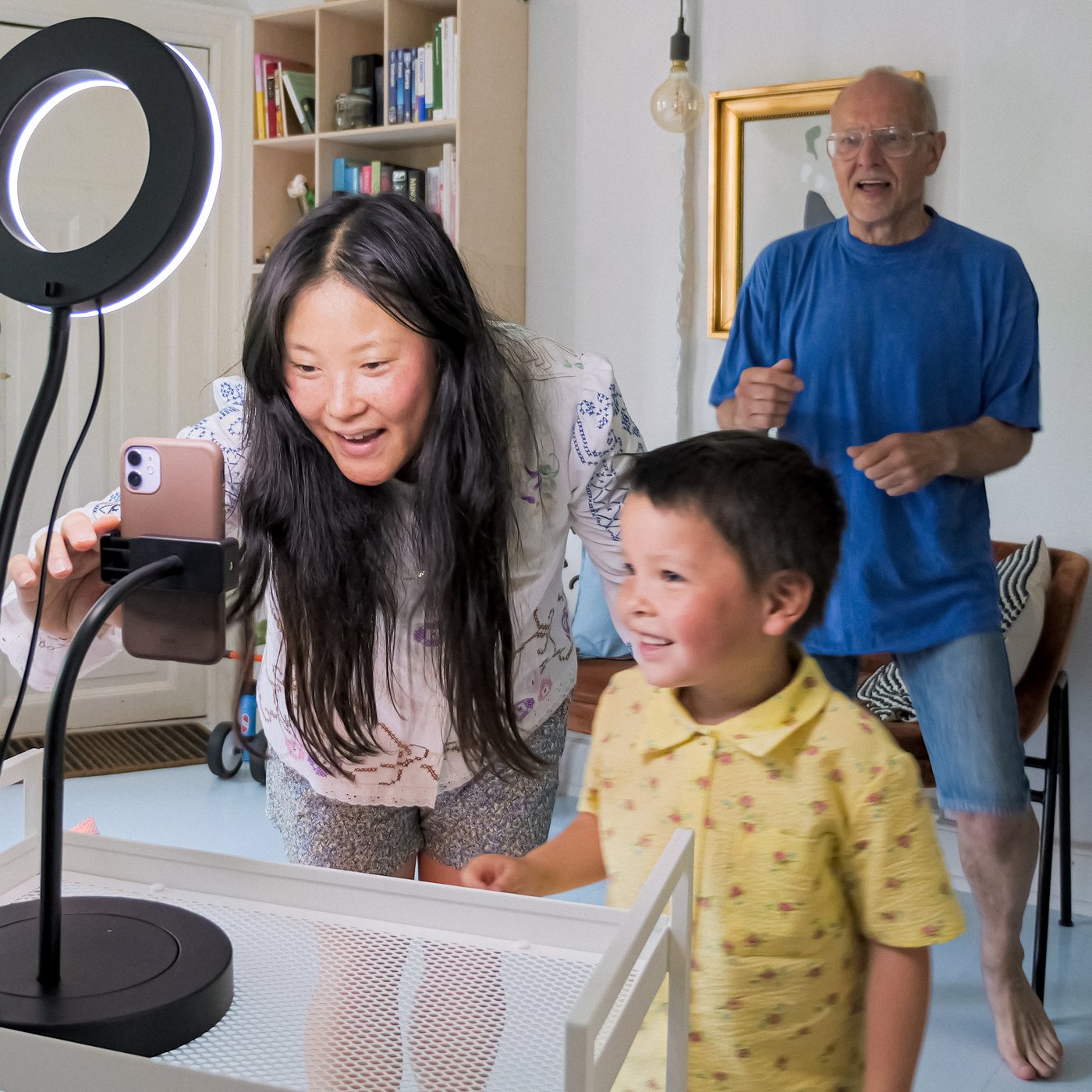 A mother and her child set up a LÅNESPELARE ring light with phone holder, ready to record a video. The father dances in the background.