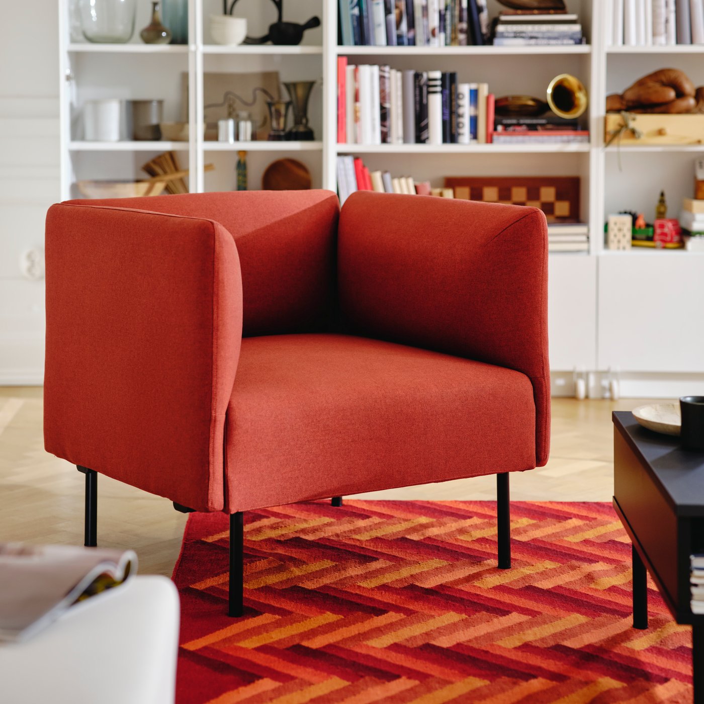 En röd LILLEHEM fåtölj i ett vardagsrum med vita bokhyllor och en röd matta.