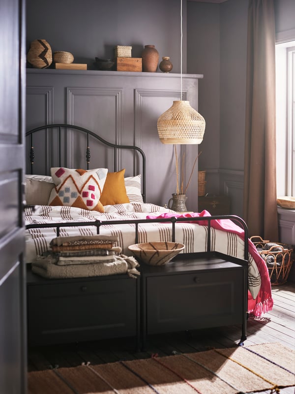 Two black storage benches and a bed with a black bed frame made with striped bed linen and a BRUNSTARR multicolor cushion.