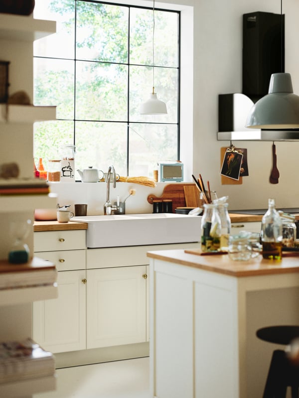 A kitchen with a kitchen island and an off/white RANARP pendant lamp above a worktop with off-white BODBYN doors below.