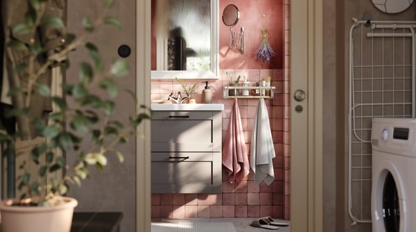 A pink-tiled bathroom with a grey ENHET cabinet with drawers, a white mirror and two towels hanging from a rail with hooks.