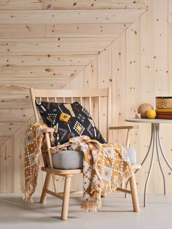 Coussin MOSSNYCKLAR et plaid SVARTFRYLE sur un fauteuil PERSBO en bouleau massif clair.