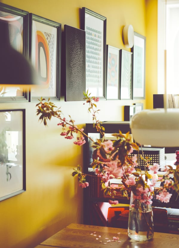 A gallery wall holding framed pictures sits on a bright yellow wall, with a SYMFONISK picture frame with WiFi speaker.