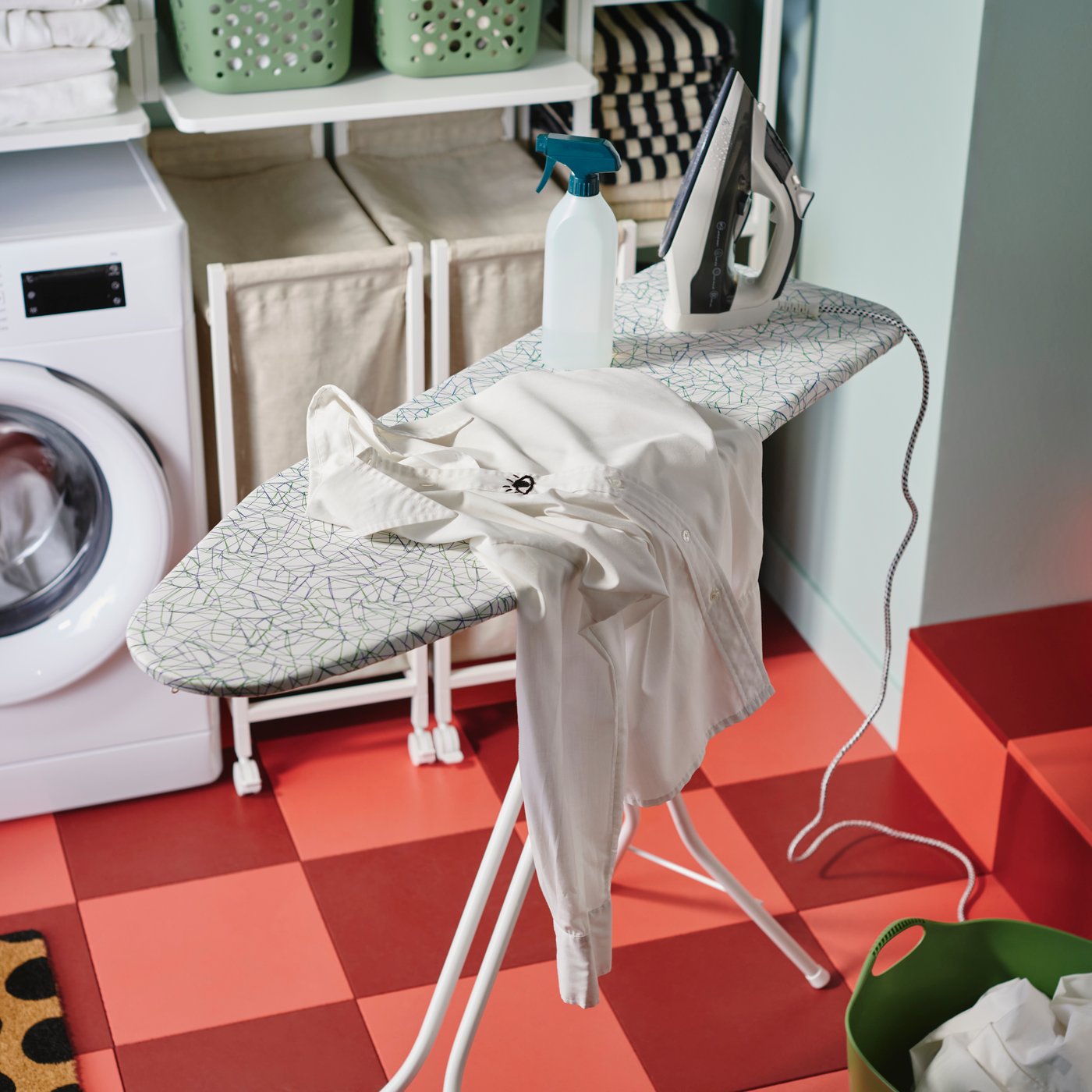 A white RUTER ironing board with a patterned cover holds a shirt and iron, in a laundry area with pink and red tiled floor.