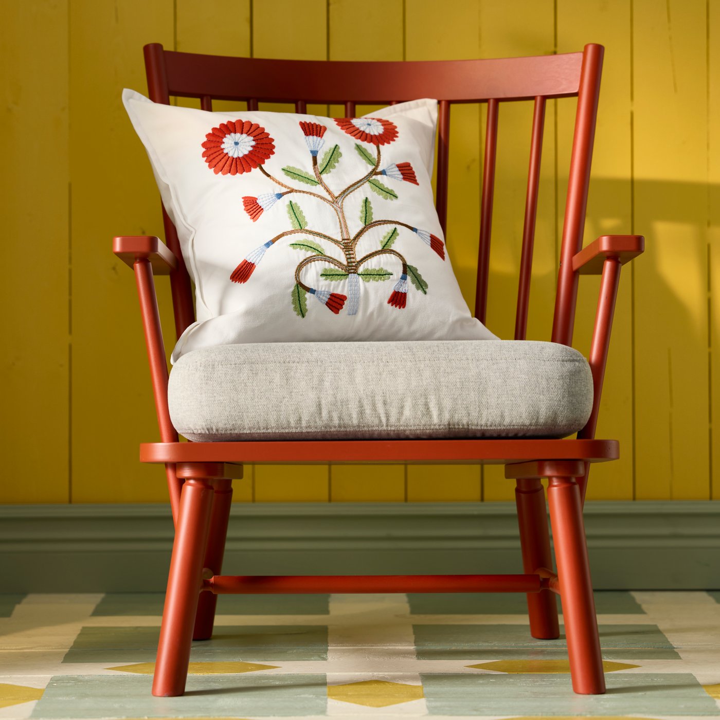 A brown-red PERSBOL armchair featuring an embroidered FACELIOR cushion cover, against a bright yellow wall.