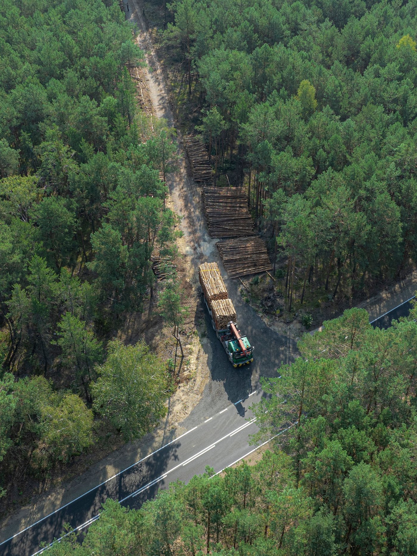Yläilmoista otettu kuva tienristeyksestä joka on ympäröity metsällä, jossa ajaa rekka, joka kuljettaa puita.