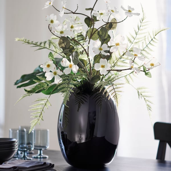 A bouquet of artificial leaves, artificial ferns and a white dogwood SMYCKA artificial spray in a STOCKHOLM 2025 vase.