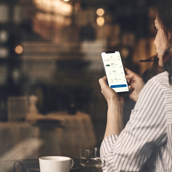 Chica en una cafetería mirando su lista de la compra en la IKEA App en su móvil