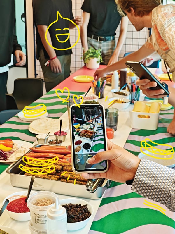 A hand holding a phone taking a picture of the tin with vegetarian and meat hot-dogs.