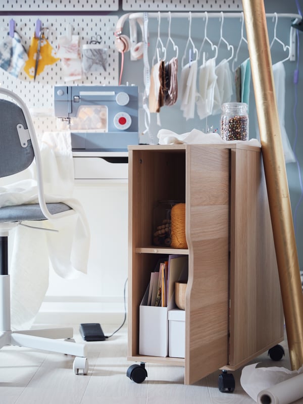 A bright room with a wheeled oak-effect ALEX storage unit is placed next to a sewing corner centred around a white ALEX desk.