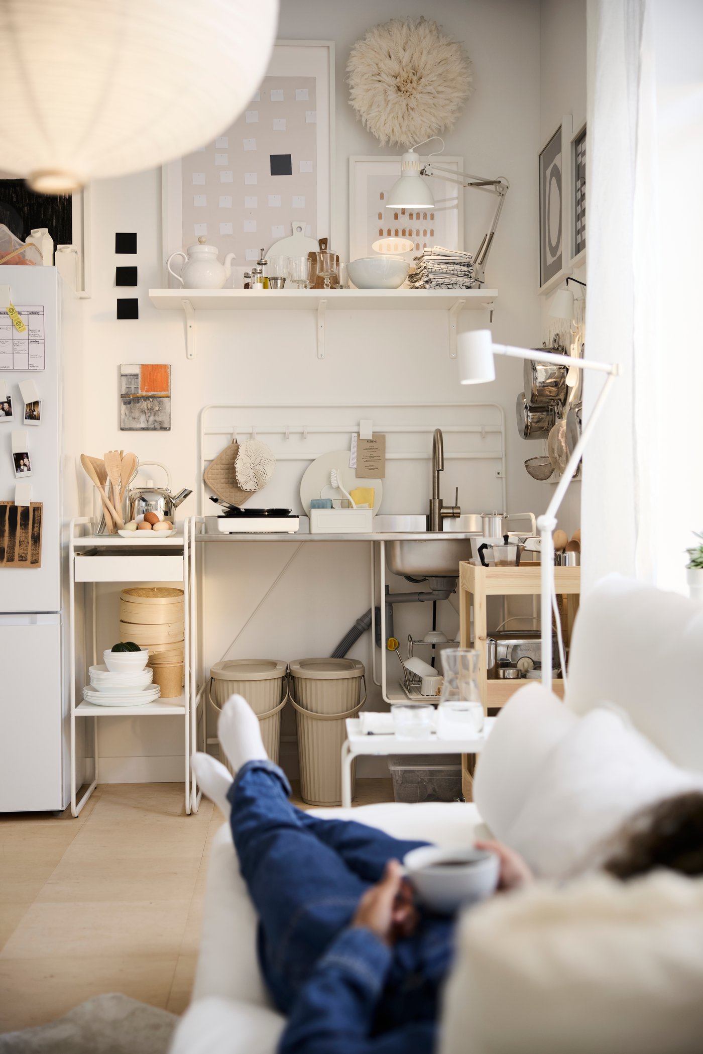 A neatly organised kitchen in the corner of a multifunctional living space. Shelves, bins and racks store and sort.