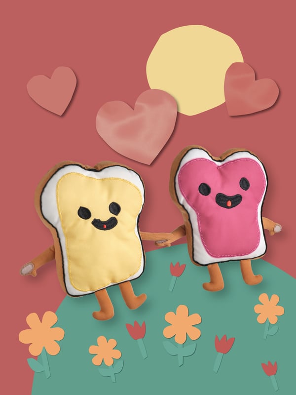 The two SAGOSKATT 2021 soft toy sandwiches holding hands on an illustrated grassy hill.