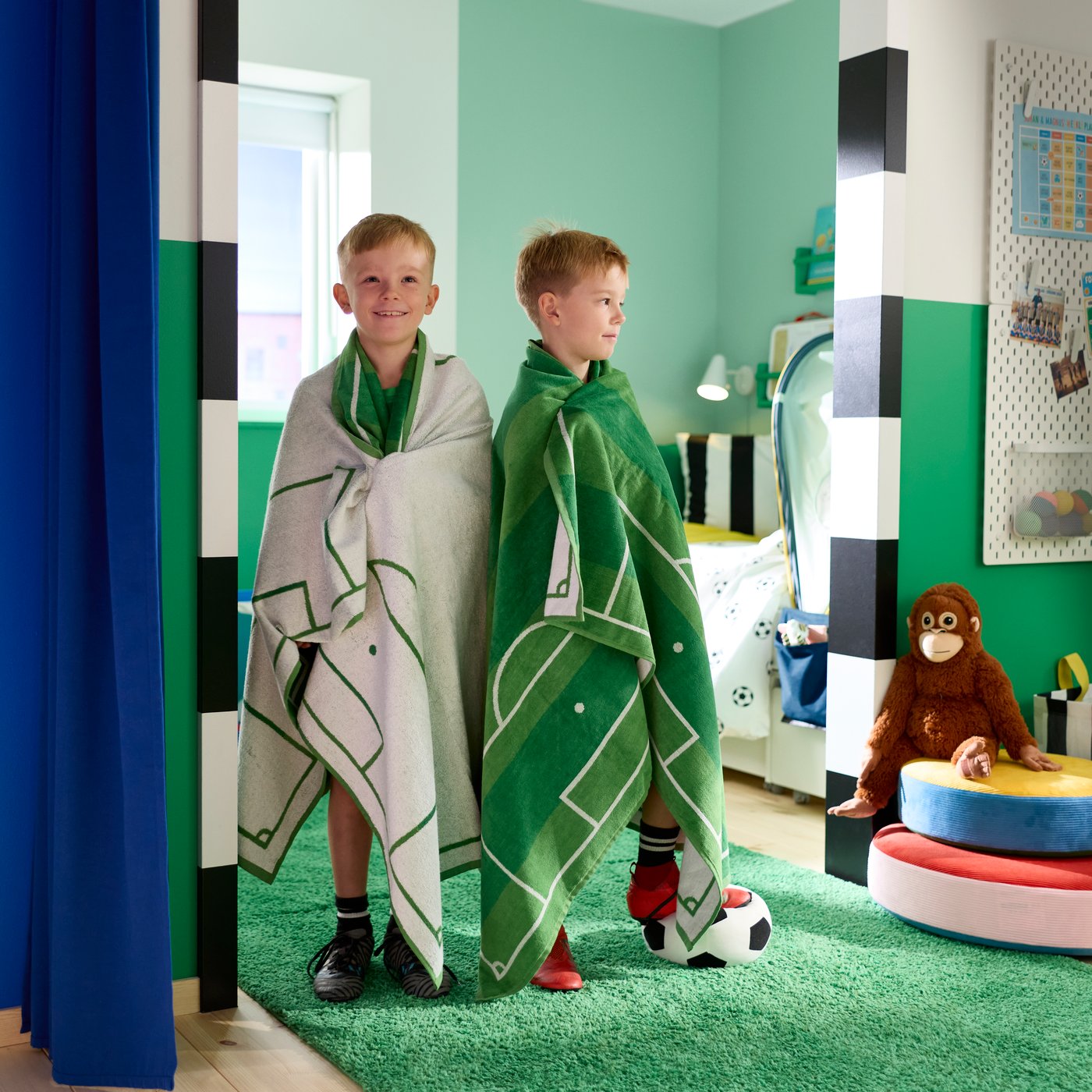 SPORTSLIG bath sheet in green with white football pitch pattern wrapped around two children in a playroom
