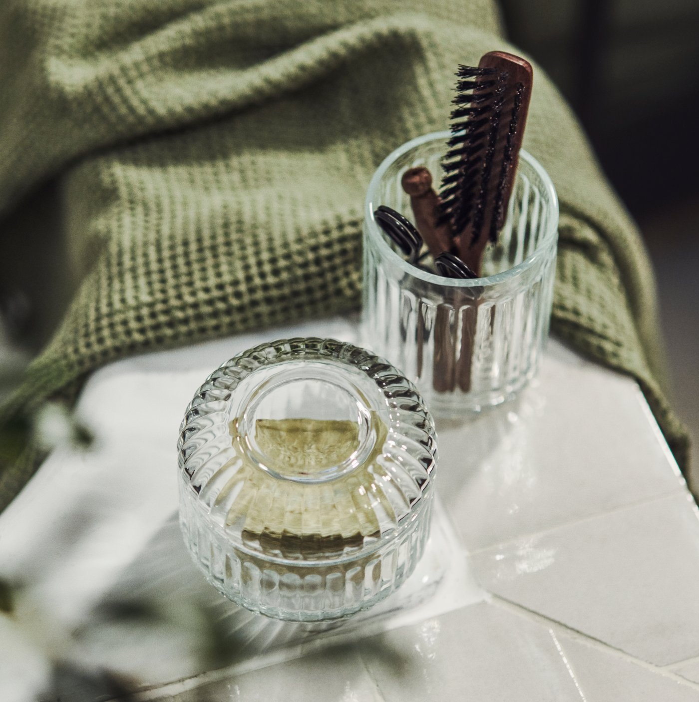 Skleněný držák na zubní kartáčky a kelímek SILVTJÄRN v koupelně. V pozadí ručník VALLASÅN.