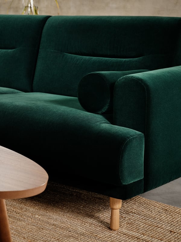 Un sillón de terciopelo verde sobre una alfombra de yute.