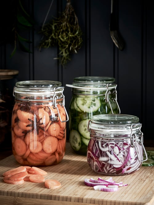 Focused shot of three jars with lid, each containing different types of vegetables, all placed on a butcher's block.