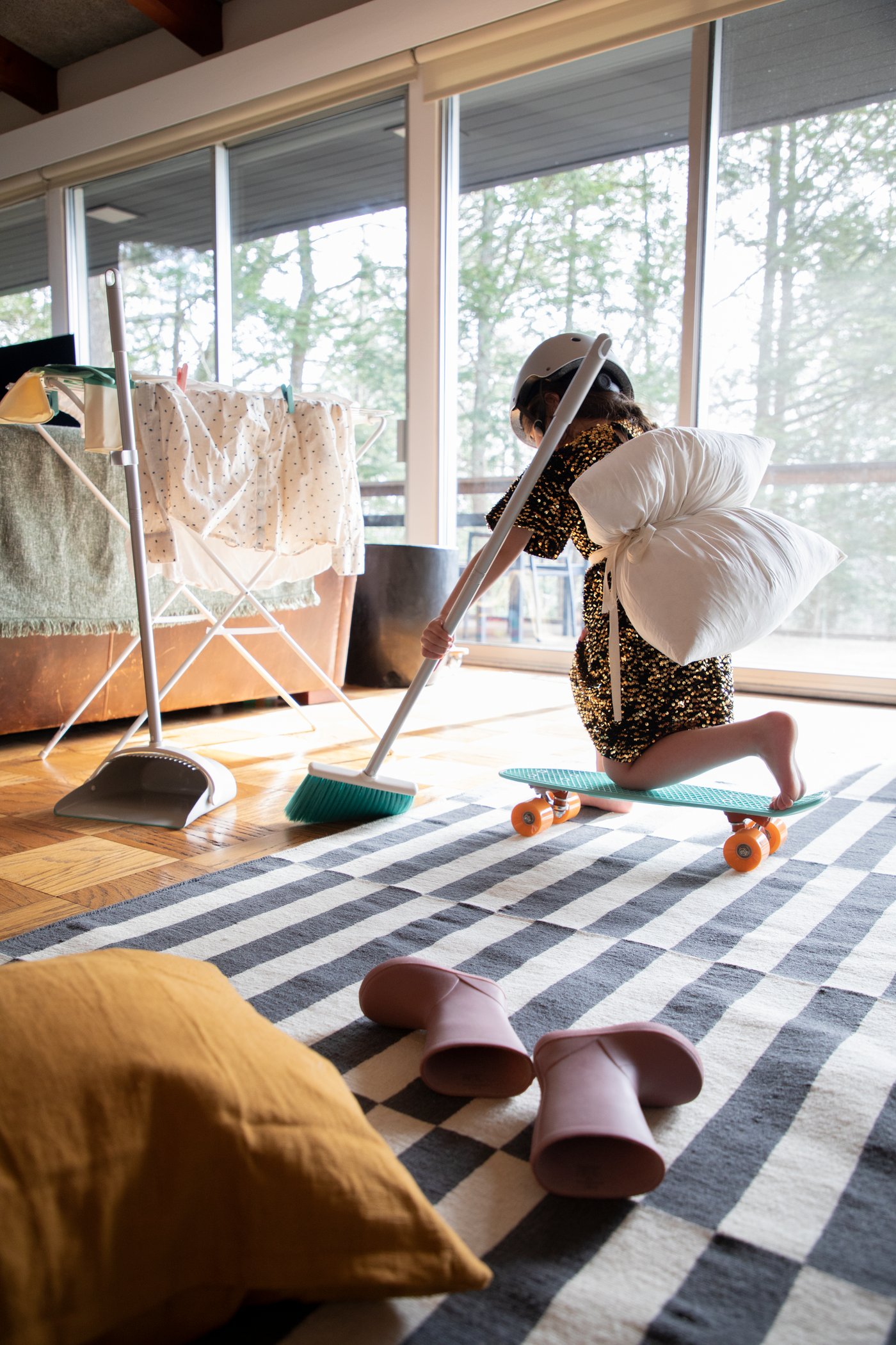 Et barn løber og fejer et gulv foran ligger et par gummistøvler smidt sammen med en gul pude.