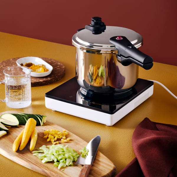 An IKEA 365+ pressure cooker in stainless steel on a TILLREDA portable induction hob in white, chopping board and knife.