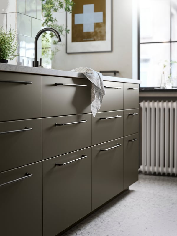 A kitchen island with brown-beige HAVSTORP kitchen fronts, black handles, a limestone effect worktop and a black kitchen tap.