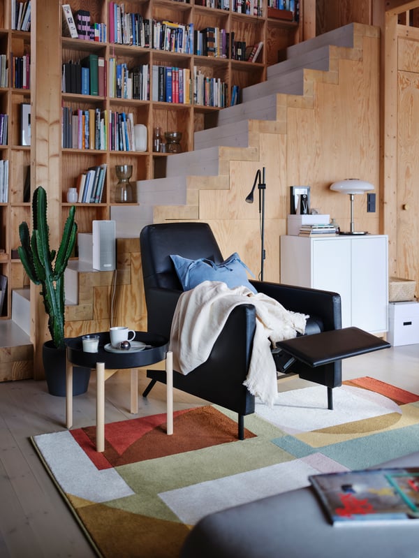 A living room with a black GISTAD recliner, a light throw, a blue cushion, and a black coffee table with a cup of tea.