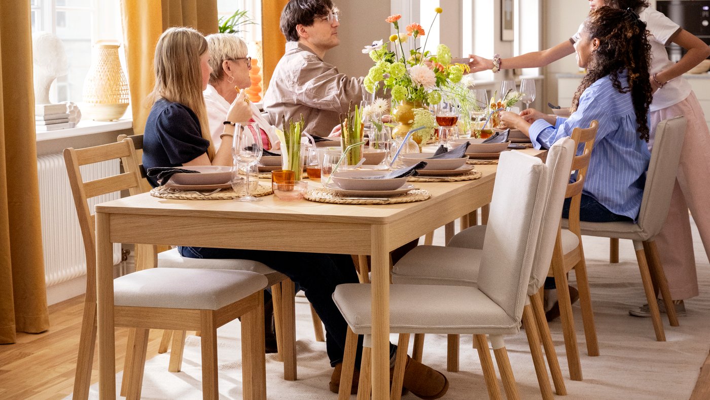 A family sitting around a TONSTAD table in oak veneer and a number of TONSTAD chairs, the table set for a festive occasion.