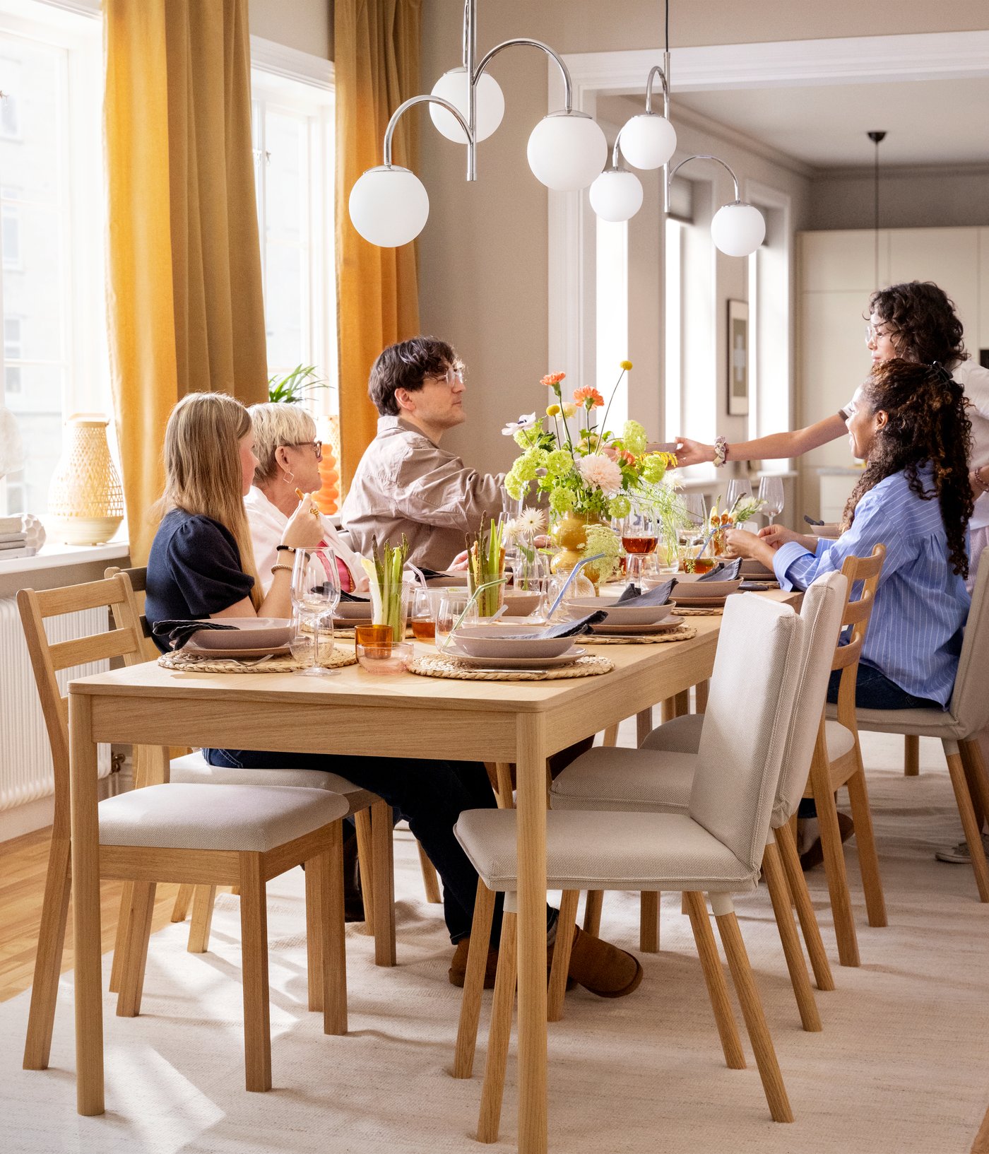 A family sitting around a TONSTAD table in oak veneer and a number of TONSTAD chairs, the table set for a festive occasion.