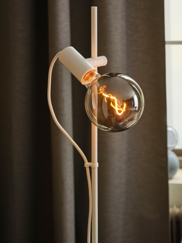 Primo piano di una lampada da terra HÅRSLINGA su una tenda marrone.