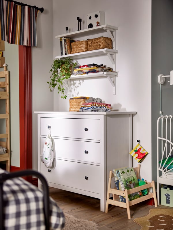 Eine weiße Kommode aus der HEMNES Serie und darüber eine TRANHULT/SANDSHULT Regalkombination an der Wand.