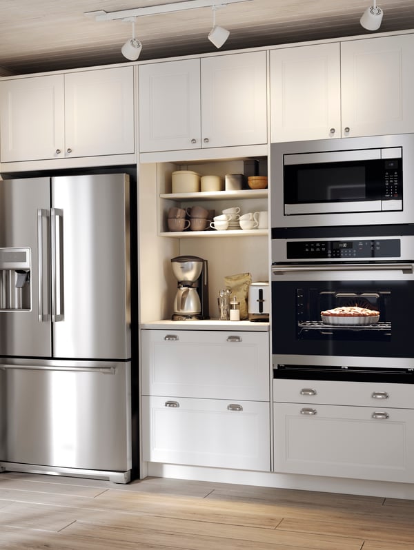 A white AXSTAD kitchen with a built-in oven and microwave and some open shelves where mugs and a coffee maker stand.