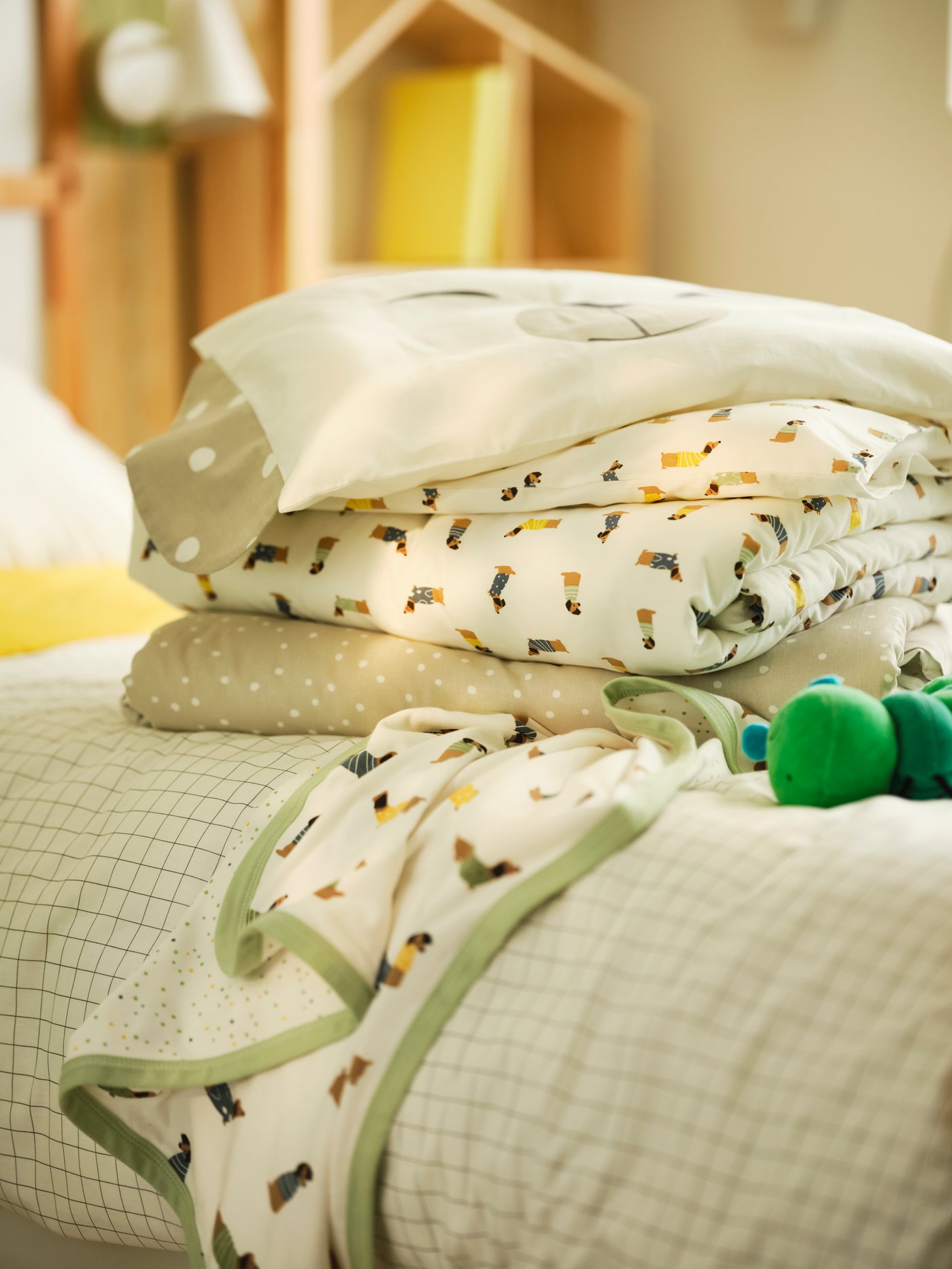 صورة مقربة لقماش DRÖMSLOTT مطوي على سرير أطفال مع غطاء لحاف. لعبة يرقانة فراشة محشوة في الجوار.