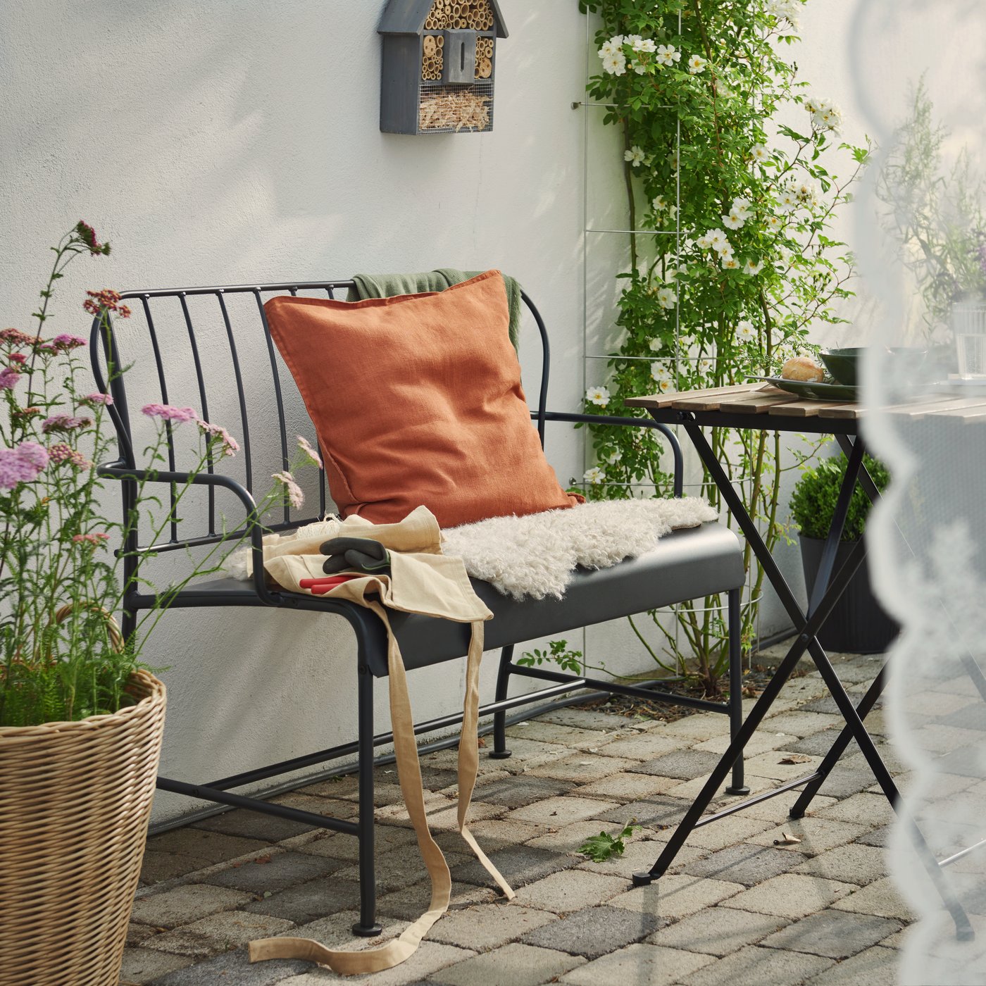 En terrasse med en grå LÄCKÖ havesofa med hynder omgiver af grønne planter på et stengulv.