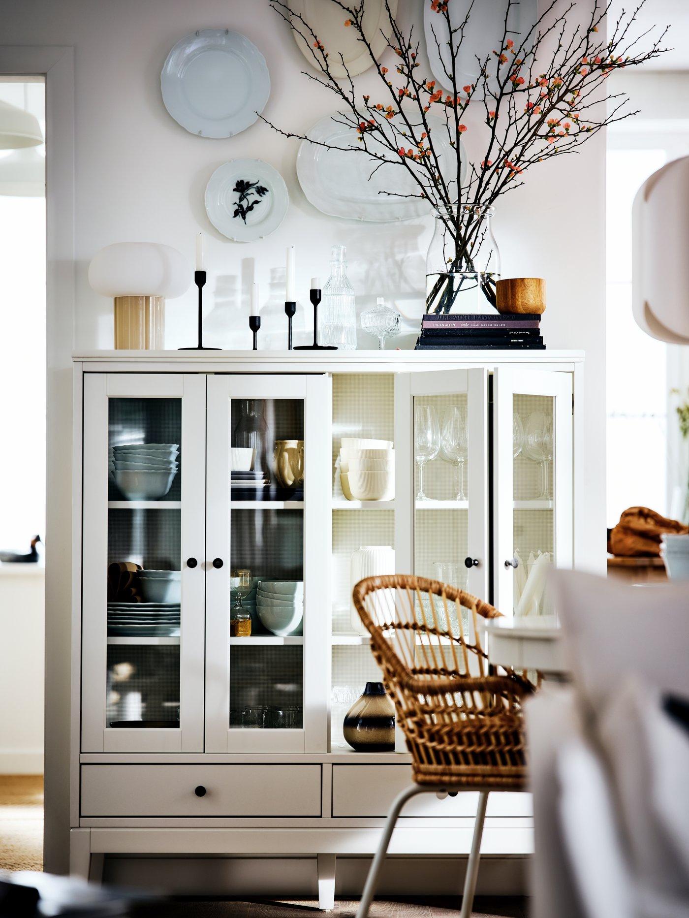 Comedor con un mueble blanco con dos puertas de vidrio plegadas de madera maciza y vidrio templado detrás de una silla beige.