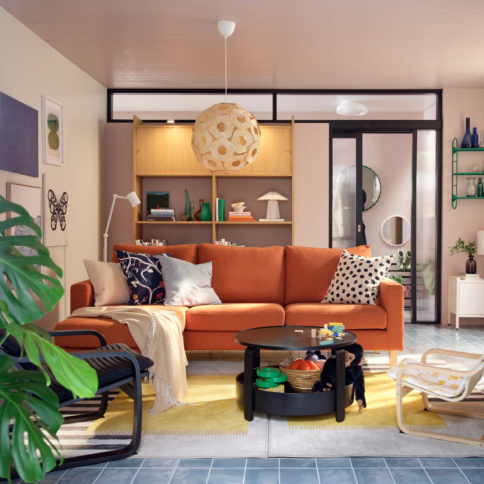 A light living room with a red-brown SALTSJÖBADEN three-seat sofa flanked by armchairs, a coffee table and toys.